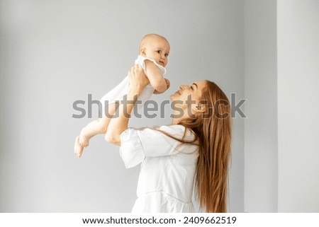 Happy cheerful young mother throws an adorable baby in air, plays, hugs baby with love, care, enjoys motherhood, maternity leave. Family spends time together.