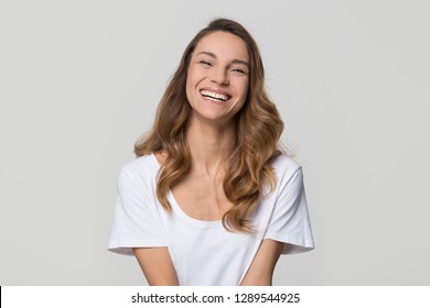 Happy Cheerful Young Woman With Beautiful Face, Teeth And Hair Laughing Looking At Camera On White Light Background, Smiling Pretty Girl Model Having Fun Isolated On Blank Grey Studio Wall, Portrait