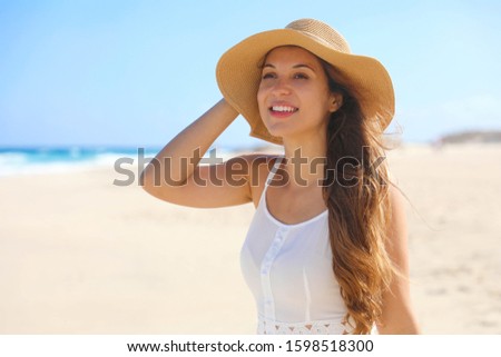 Happy cheerful young woman with straw hat walking on the beach