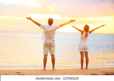 Happy Cheering Couple Enjoying Sunset At Beach With Arms Raised Up In Joyful Elated Happiness. Happiness Concept With Young Joyous Couple, Caucasian Man And Asian Woman.