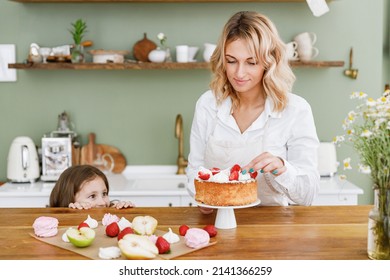 Happy Chef Cook Baker Mom Woman In White Shirt Work With Baby Girl Helper Hiding Behind Table At Kitchen Table Home. Cooking Food Process Concept Mommy Little Kid Daughter Prepare Fruit Sweet Pie Cake