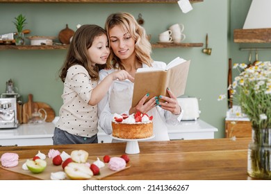 Happy Chef Cook Baker Mom Woman In Pastel Apron Work Book Of Recipes Child Baby Girl Helper At Kitchen Table Home Cooking Food Process Concept Mommy Little Kid Prepare Cake Mother's Day Family Concept