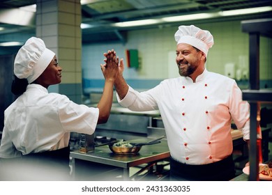 Happy chef giving high five to his African American cook assistant while working in the kitchen. - Powered by Shutterstock