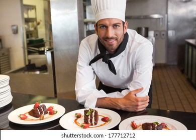 Happy chef looking at camera behind counter of desserts in a commercial kitchen - Powered by Shutterstock