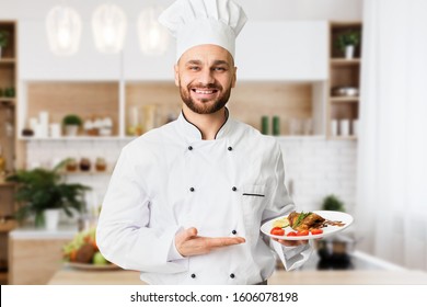 Happy Chef Man Holding Plate With Roasted Chicken Serving Dish Standing In Restaurant Kitchen. Selective Focus