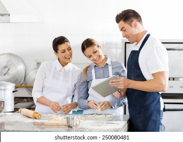 Happy chefs checking recipe on digital tablet while preparing pasta in commercial kitchen - Powered by Shutterstock