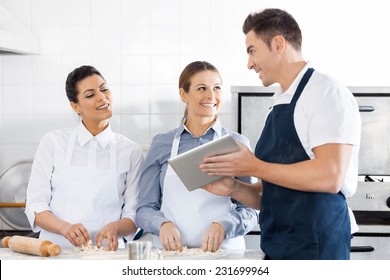 Happy chefs discussing recipe on digital tablet while preparing pasta in commercial kitchen - Powered by Shutterstock