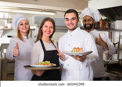 Happy Chefs And Young Smiling Nippy In Apron Working At Restaurant Kitchen. Selective Focus
