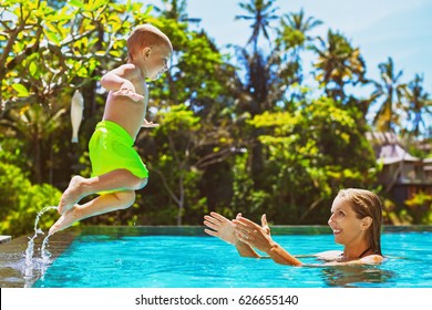 Happy Child In Action - Active Kid Swim With Fun In Swimming Pool. Baby Son Jump High To Mother Catching Hands. Healthy Family Lifestyle, Summer Vacation Water Sports Activity And Lesson With Parents
