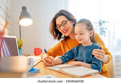 Happy child and adult are sitting at desk. Girl doing homework or online education.