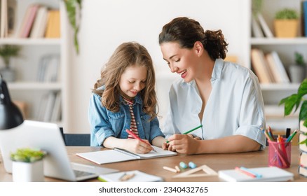 Happy child and adult are sitting at desk. Girl doing homework or online education. - Shutterstock ID 2340432765