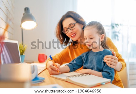 Happy child and adult are sitting at desk. Girl doing homework or online education.