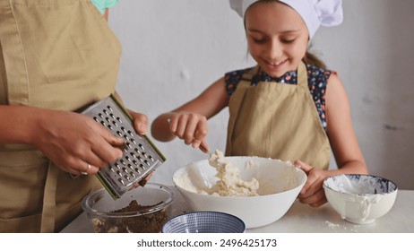 Happy child and adult wearing aprons, cooking together in kitchen. The adult grates chocolate while the child mixes batter in a bowl. Enjoying baking time. - Powered by Shutterstock