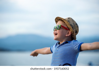 Happy Child Against Blue Sky Background. Summer Vacation Concept. Kid In Sunglasses And Hat. Boy With Big Smile.