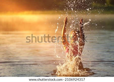 A happy child is bathing in the water . The girl splashes water in the river . Happy childhood . Children 's summer holidays . Outdoor play