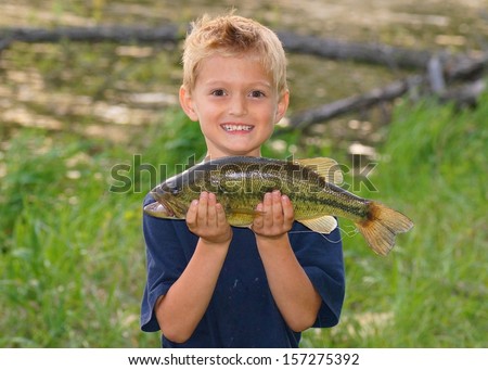 Happy child with a big fish he caught next to a pond