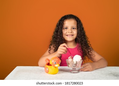 Happy Child With A Bowl Of Ice Cream On A Table With Orange Background, Selective Focus.