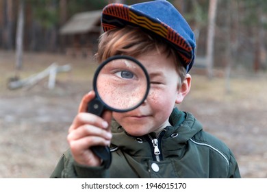 Happy child boy exploring nature with magnifying glass. Kid discovering world in part on spring and summer time. Forest school.
