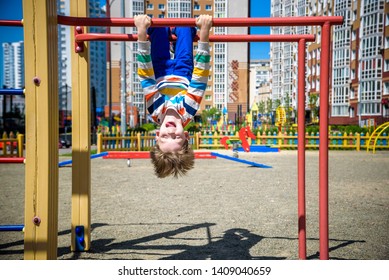 Happy child boy hanging upside down on bar, playground in city, outdoor activities