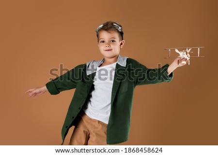 happy child boy playing with wooden toy airplane on studio background. dream of becoming a pilot