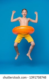 Happy Child Boy In Swimsuit Jumping With Swimming Ring, Blue Studio Background