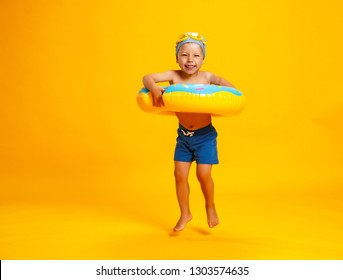 Happy Child Boy In Swimsuit With Swimming Ring Donut On A Colored Yellow Background
