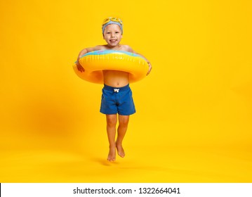 Happy Child Boy In Swimsuit With Swimming Ring Donut On A Colored Yellow Background
