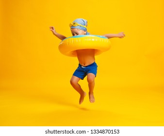 Happy Child Boy In Swimsuit With Swimming Ring Donut On A Colored Yellow Background
