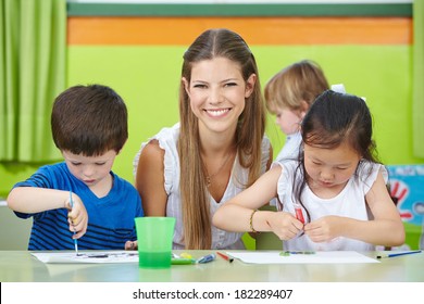 Happy Child Care Worker With Children Drawing In A Kindergarten