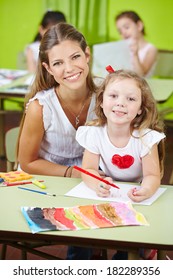 Happy Child Care Worker Helping Girl Painting In A Kindergarten