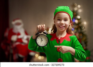 Happy Child In Christmas Elf Costume With Alarm.