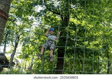 Happy child climbing on a rope course in the forest wearing a blue helmet on a sunny day. Concept of active lifestyle, outdoor adventure, and physical challenges for kids in nature. High quality photo - Powered by Shutterstock