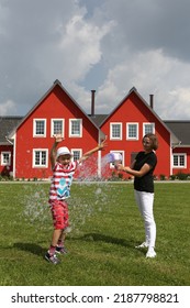 Happy Child, Cute Kid, Boy With Mother Plays. Summer Active Rest, Outdoor Recreation With Soap Bubbles. Family Recreation With Soap Bubbles In Fishing Village Hotel In Ryazan, Russia. Red Houses, Home