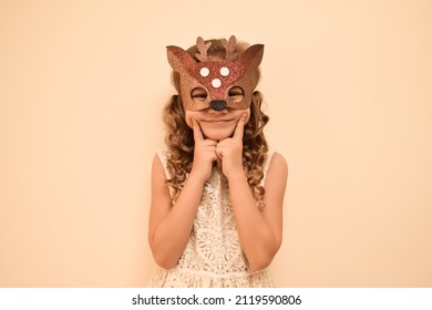 Happy child in deer costume. Little cute girl in a carnival masquerade deer mask made of shiny glitter foamiran on a beige background. The child is preparing for the masquerade.