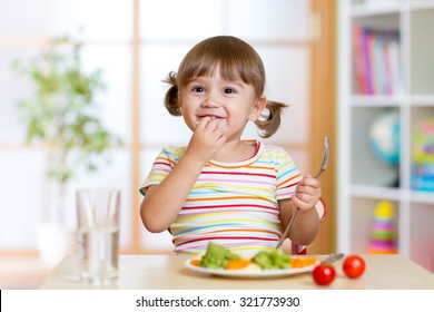 Happy child eats vegetables sitting at table in nursery