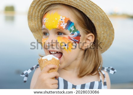 Happy child with face art paint eating ice-cream at summertime