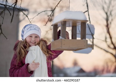 Happy Child Girl With Bird Feeder In Winter Garden