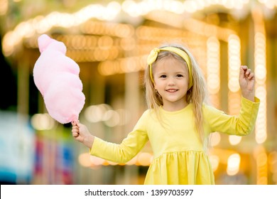 Happy Child Girl With Cotton Candy At An Amusement Park. The Concept Of The International Children's Day. Happy Healthy Child In The Summer