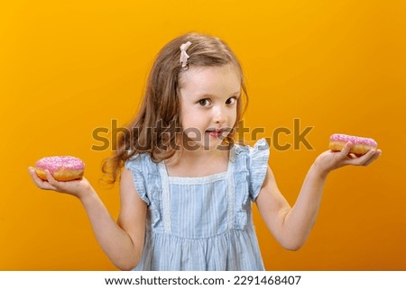 a happy child a girl in a dress holds donuts in her hands on the yellow background