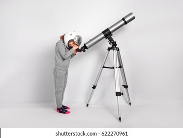 Happy Child Girl Dressed In An Astronaut Costume Looks Through A Big Telescope