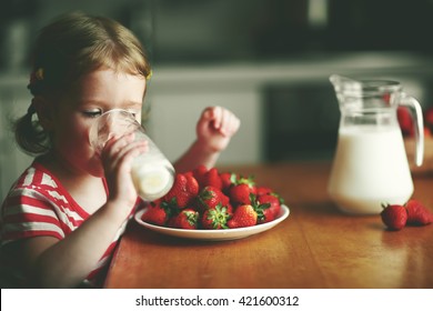 hạnh phúc con gái uống sữa và ăn dâu tây trong nhà bếp mùa hè