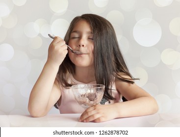 Happy Child Girl Eating Ice Cream In White And Chocolate Bowl On Light Background. Enjoying Delicious.