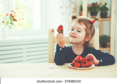 happy child girl eats strawberries in the summer home kitchen