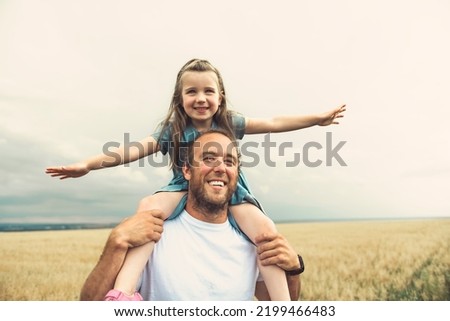 A happy child girl and father are playing in wheat field.