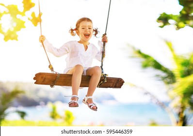 Happy child girl laughing and swinging on a swing at the beach near the ocean in summer