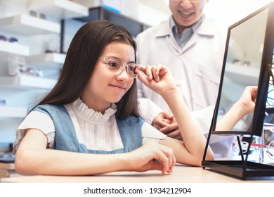 Happy Child Girl With New Optical Glasses, Child Girl  Trying On Spectacles, With An Optometrist Giving Advice Beside