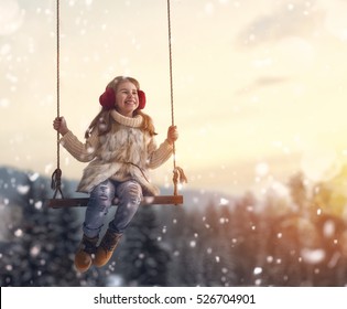 Happy Child Girl On Swing In Sunset Winter. Little Kid Playing On A Winter Walk In Nature.