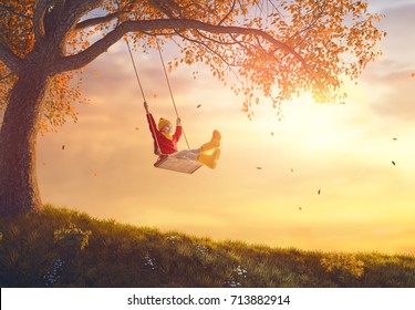 Happy child girl on swing in sunset fall. Little kid playing in the autumn on the nature walk.