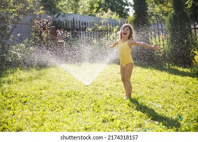 Happy Child Girl Playing With Garden Hose And Having Fun With Spray Of Water In Sunny Backyard. Summer Time. Kid Boy Helps Water Garden With Hose. Slow Life. Enjoying The Little Things. Summer Holiday