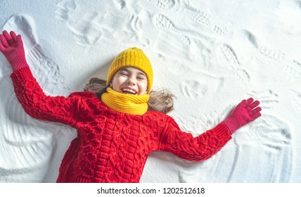 Happy Child Girl Playing On A Winter Walk In Nature. Kid Making Snow Angel.